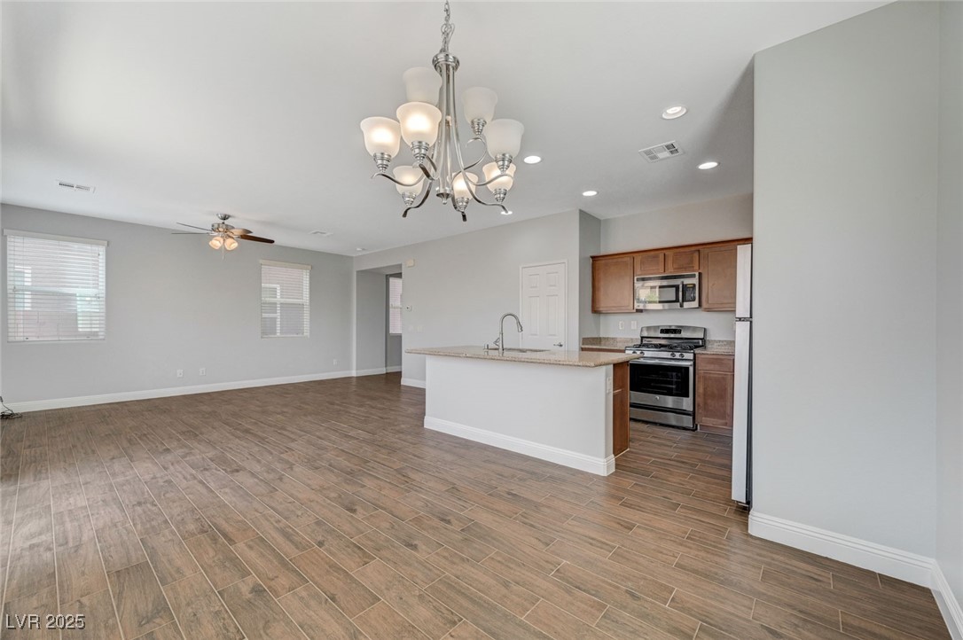 5377 Panaca Spring Street Las Vegas, NV 89122 - Photo 15 of 59 Kitchen with hanging light fixtures, stainless steel appliances, a chandelier, an island with sink, and brown cabinetry