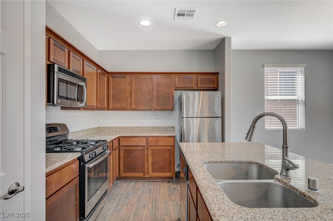 5377 Panaca Spring Street Las Vegas, NV 89122 - Photo 19 of 59 Kitchen with stainless steel appliances, brown cabinets, wood finish floors, light stone countertops, and recessed lighting