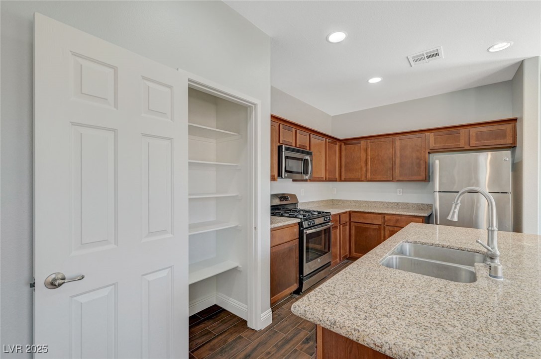 5377 Panaca Spring Street Las Vegas, NV 89122 - Photo 22 of 59 Kitchen featuring stainless steel appliances, brown cabinetry, wood tiled floors, recessed lighting, and light stone counters