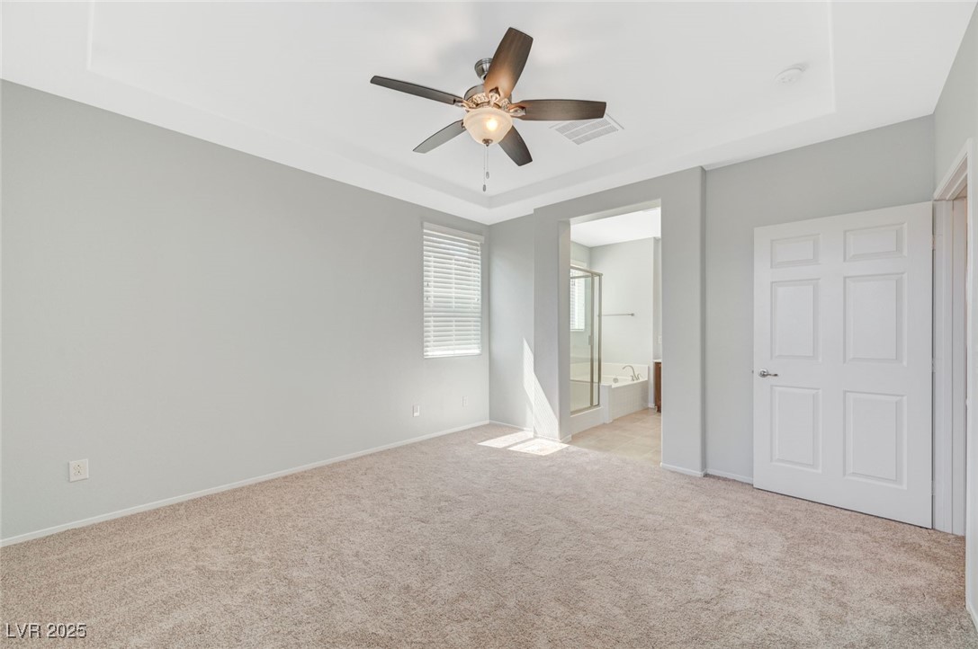 5377 Panaca Spring Street Las Vegas, NV 89122 - Photo 28 of 59 Unfurnished bedroom featuring a raised ceiling, light colored carpet, ensuite bathroom, and a ceiling fan
