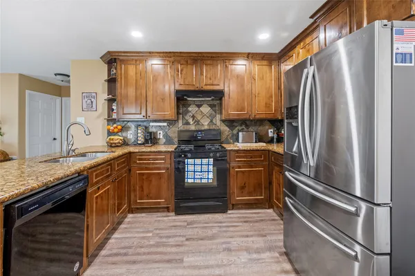 a kitchen with granite countertop wooden floors stainless steel appliances a sink cabinets and a window