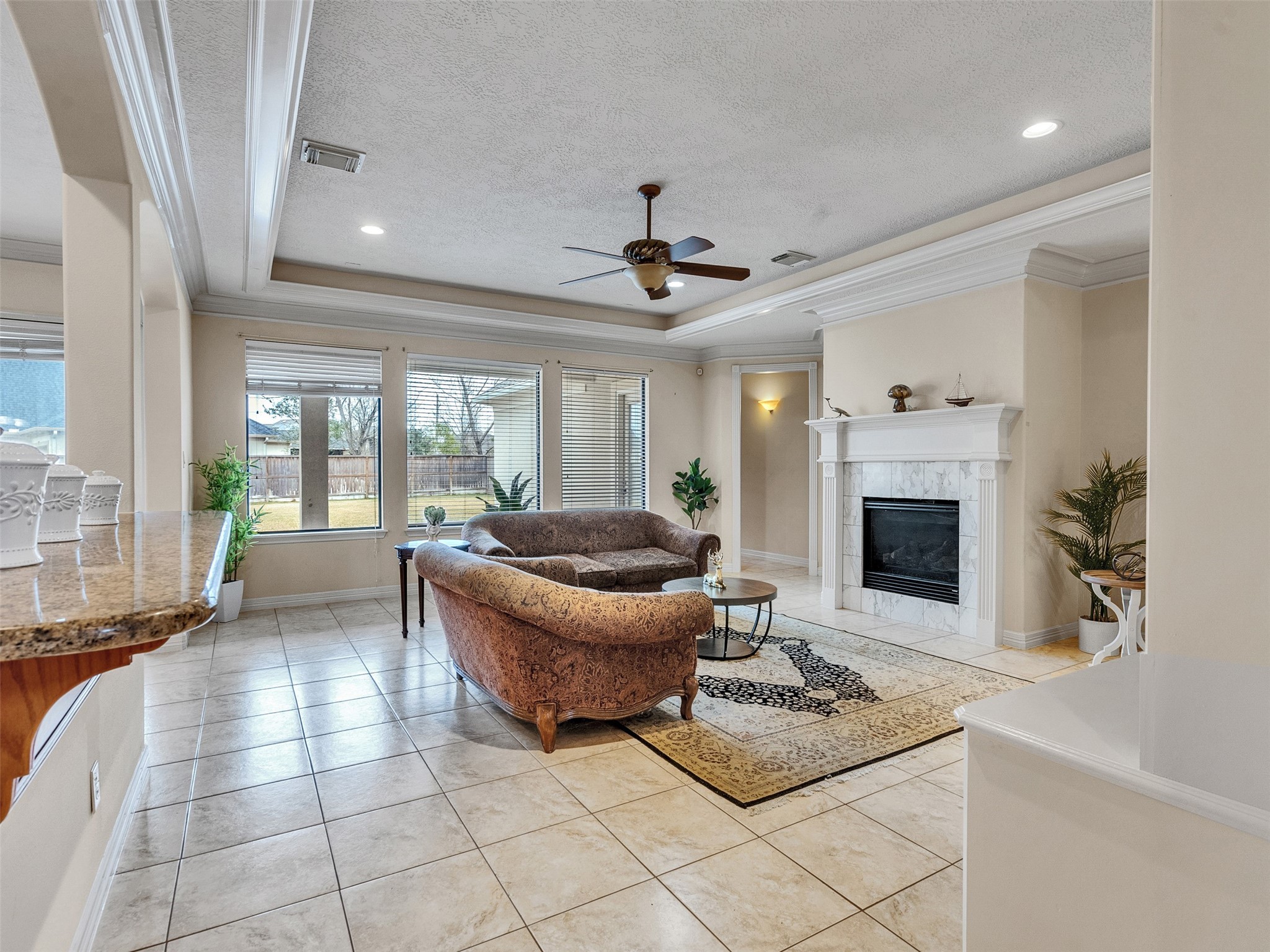 6914 Sandwedge Point Court Spring, TX 77389 - Photo 16 of 50 This elegant living room features a cozy fireplace, large windows with ample natural light, and a ceiling fan. The space is adorned with a plush sofa set and tasteful decor, offering a welcoming and comfortable atmosphere.