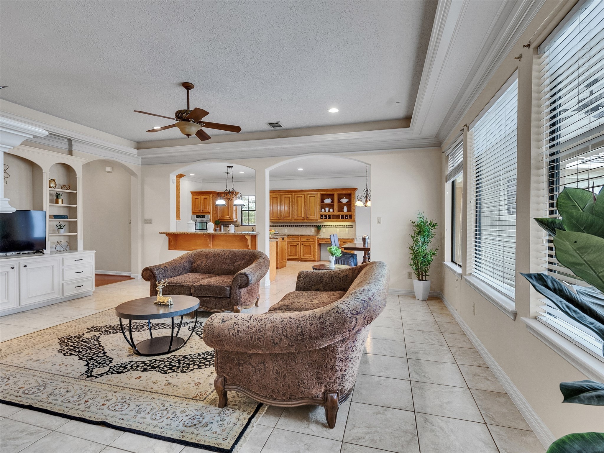 6914 Sandwedge Point Court Spring, TX 77389 - Photo 19 of 50 This spacious living area features large windows for natural light, tiled flooring, and a cozy seating arrangement. It flows into an open kitchen with wooden cabinetry and a breakfast bar, offering a welcoming atmosphere for family gatherings.