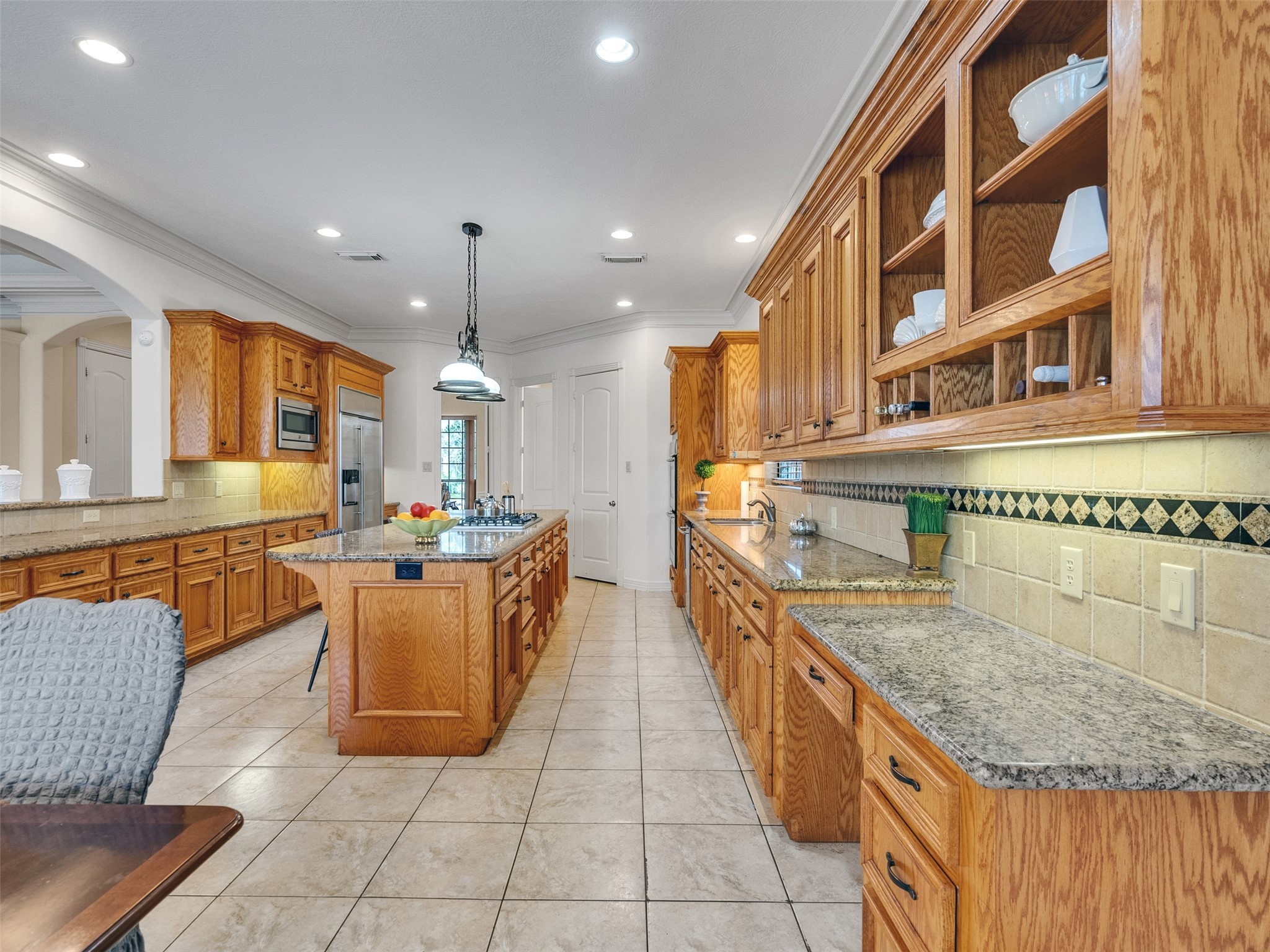 6914 Sandwedge Point Court Spring, TX 77389 - Photo 23 of 50 This photo showcases a spacious kitchen with ample wooden cabinetry, granite countertops, and a central island. The room features tiled flooring, recessed lighting, and modern appliances, offering a warm and functional cooking space.