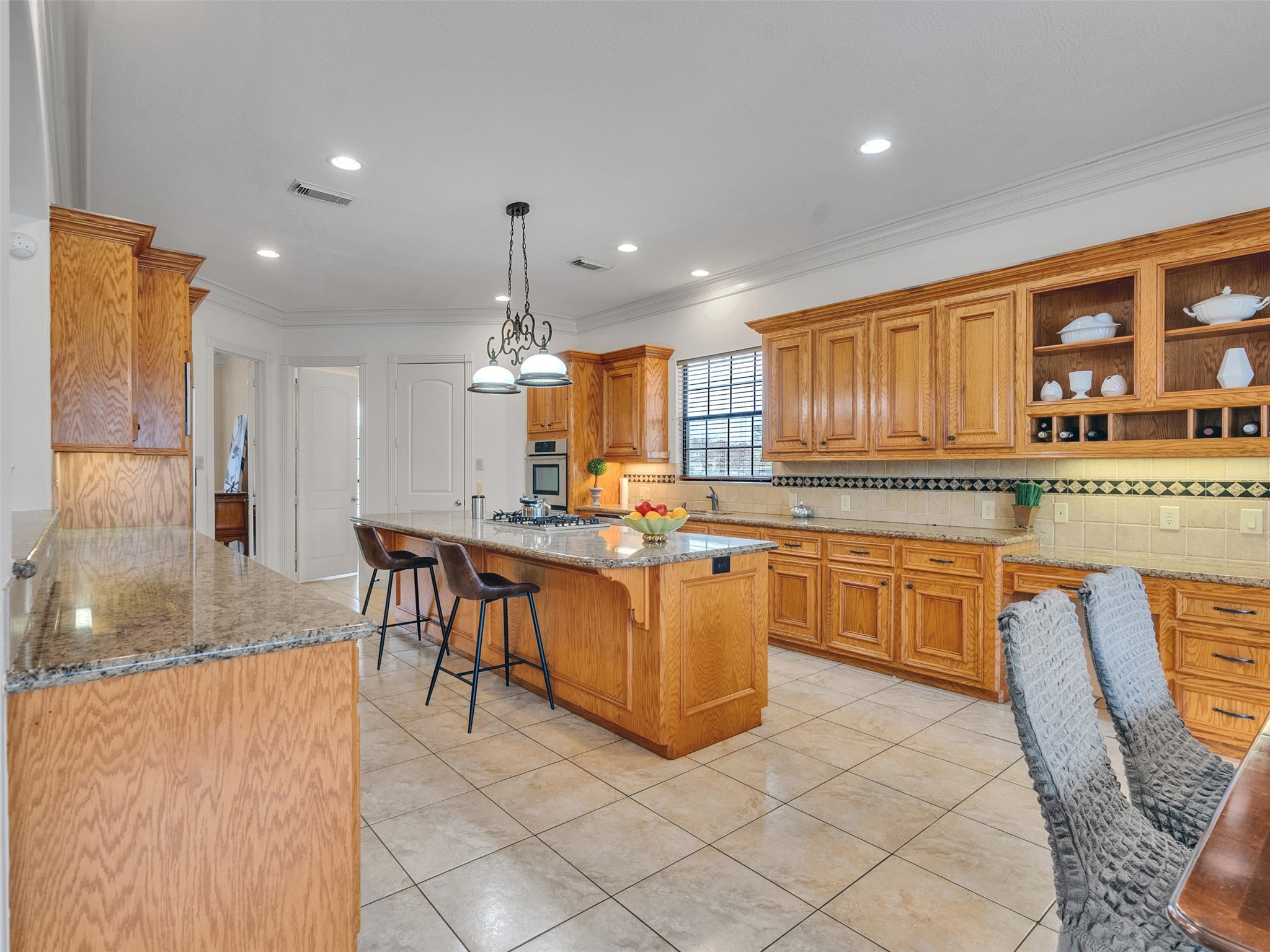 6914 Sandwedge Point Court Spring, TX 77389 - Photo 24 of 50 This spacious kitchen features warm wood cabinetry, granite countertops, and a large island with a gas cooktop. It's well-lit with recessed lighting and a stylish pendant fixture, complemented by tile flooring and a cozy seating area.