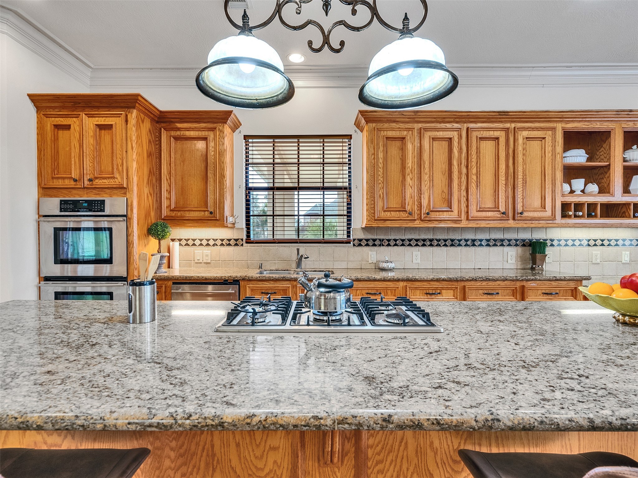 6914 Sandwedge Point Court Spring, TX 77389 - Photo 25 of 50 This spacious kitchen features granite countertops, a central island with a gas cooktop, and warm wood cabinetry. It includes double ovens, ample storage, and a classic tile backsplash, creating a welcoming and functional space.