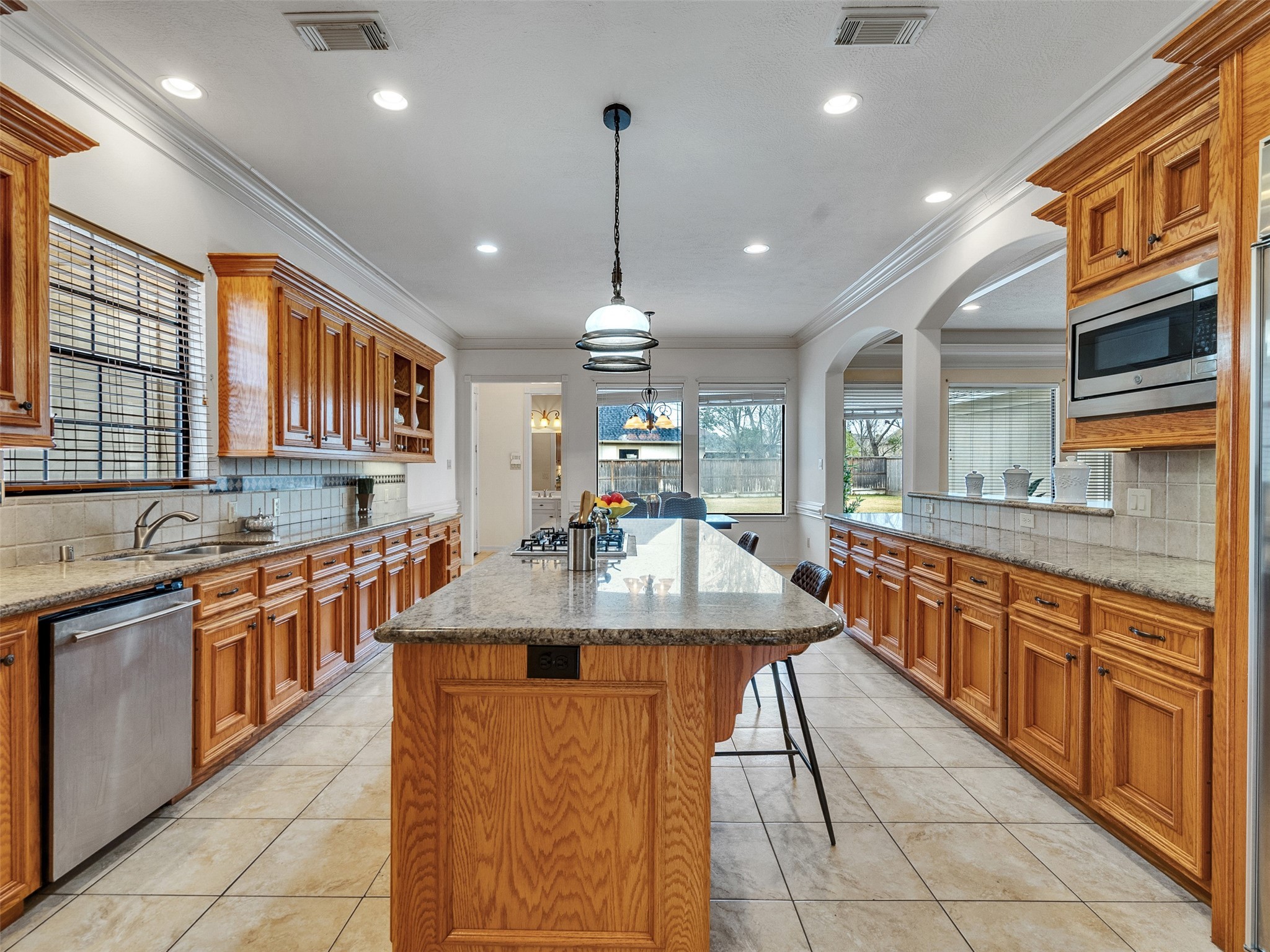 6914 Sandwedge Point Court Spring, TX 77389 - Photo 28 of 50 This spacious kitchen features warm wood cabinetry, granite countertops, and a large central island with seating. It offers ample storage and modern appliances, creating a welcoming space for cooking and entertaining. Large windows provide plenty of natural light and a view of the backyard.