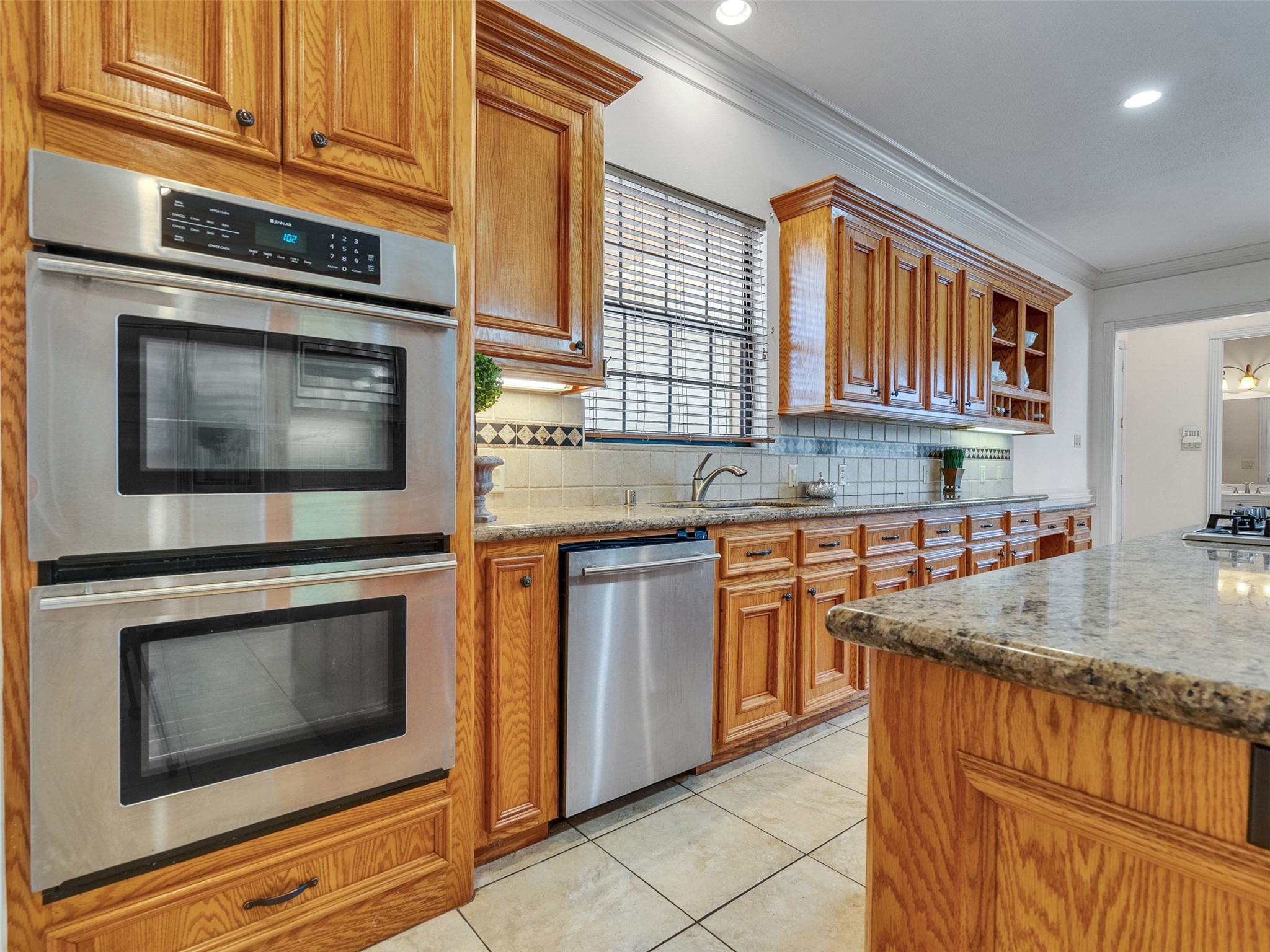 6914 Sandwedge Point Court Spring, TX 77389 - Photo 30 of 50 Spacious kitchen with warm wooden cabinetry, stainless steel double ovens, and granite countertops. Features a tile backsplash, under-cabinet lighting, and ample natural light from a large window above the sink.