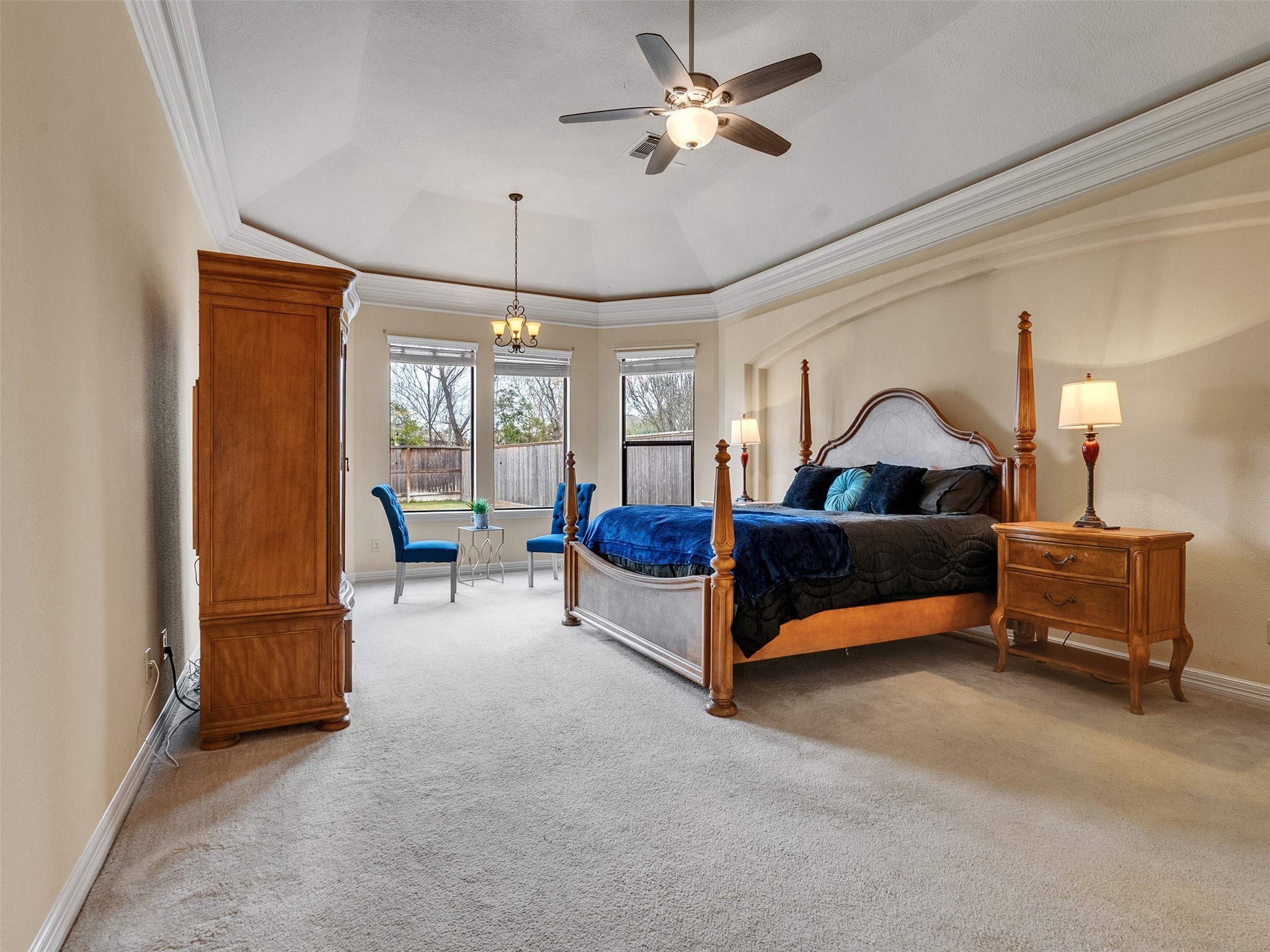 6914 Sandwedge Point Court Spring, TX 77389 - Photo 32 of 50 This spacious Master Bedroom features a tray ceiling with a fan, large windows providing natural light, and elegant furniture including a four-poster bed and matching wooden pieces. Cozy and inviting, it also offers a small seating area by the windows.