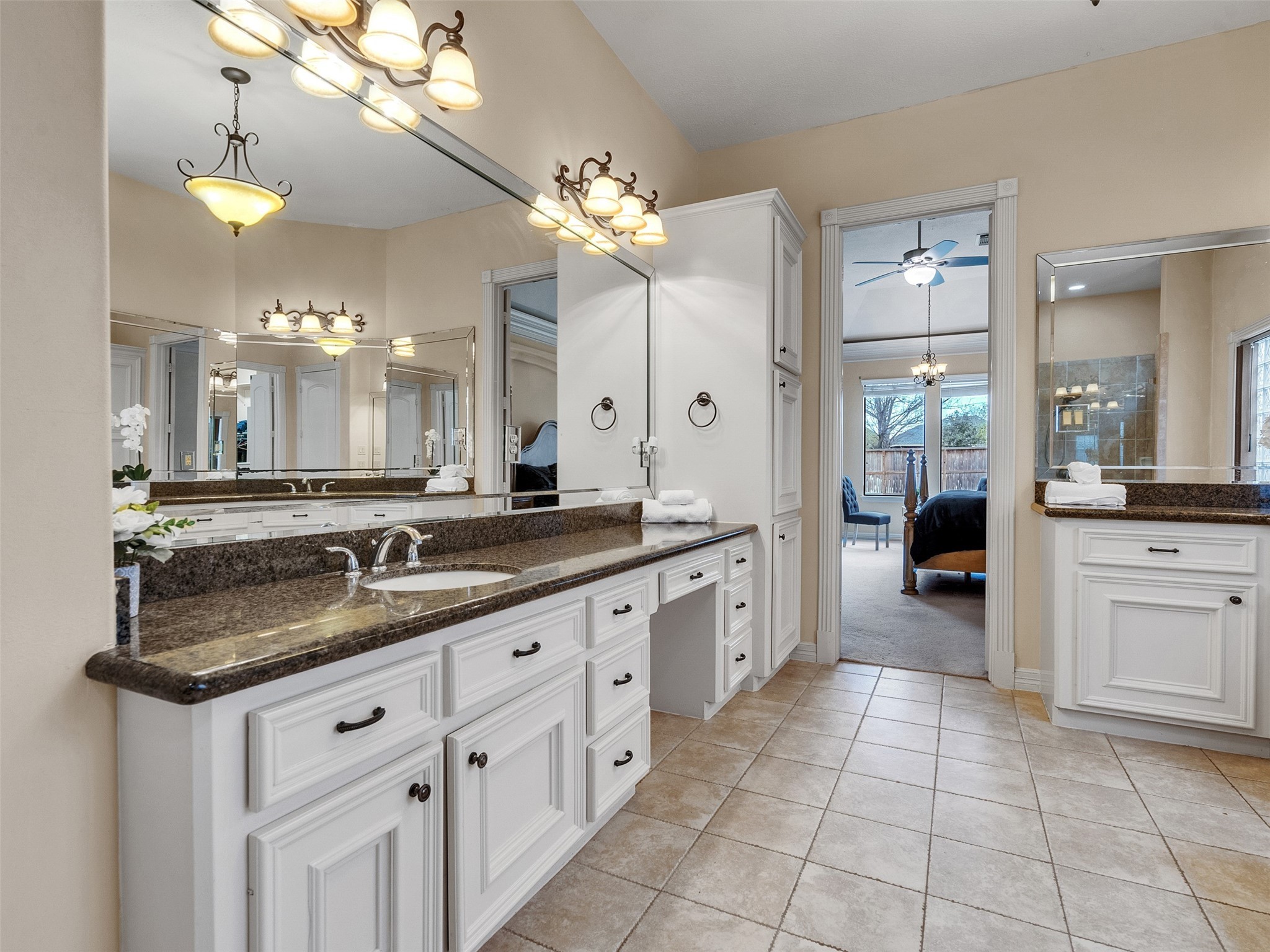6914 Sandwedge Point Court Spring, TX 77389 - Photo 34 of 50 This bathroom features dual sinks with granite countertops, ample cabinetry, elegant lighting fixtures, and a large mirror. It opens into a cozy bedroom with a ceiling fan and natural light from multiple windows.