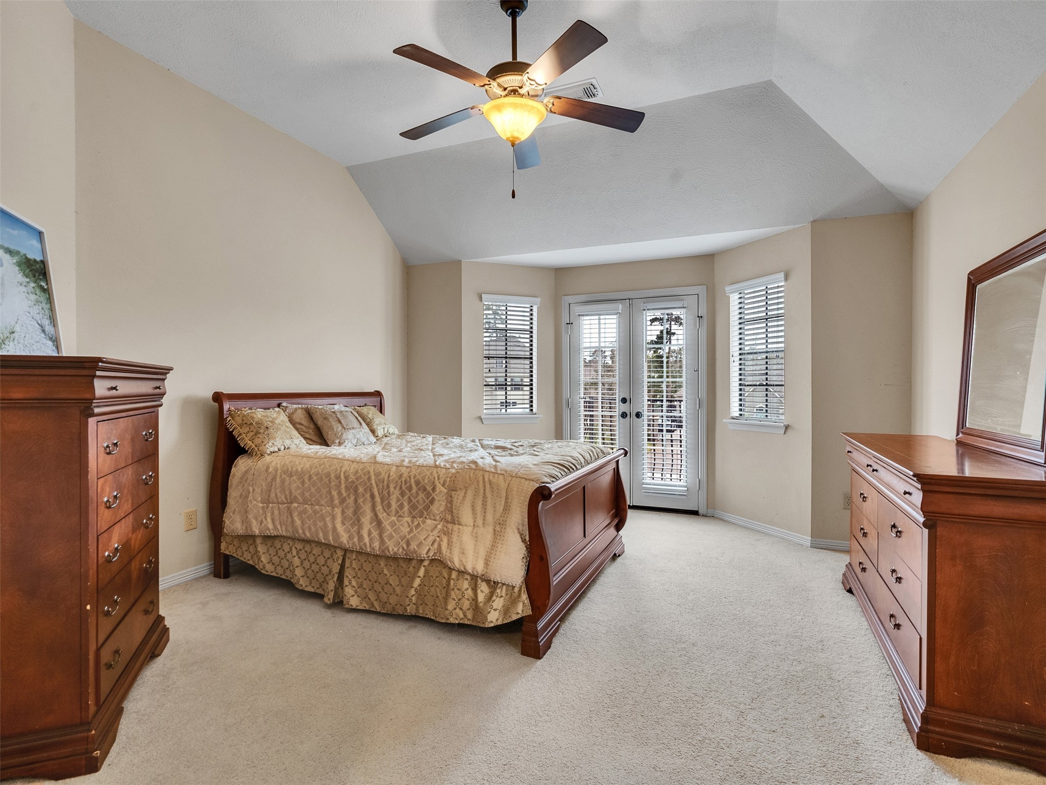 6914 Sandwedge Point Court Spring, TX 77389 - Photo 36 of 50 Spacious bedroom with a vaulted ceiling and neutral tones. Features a ceiling fan and natural light from large windows and French doors. Includes elegant wooden furniture and plush carpeting for a cozy feel.