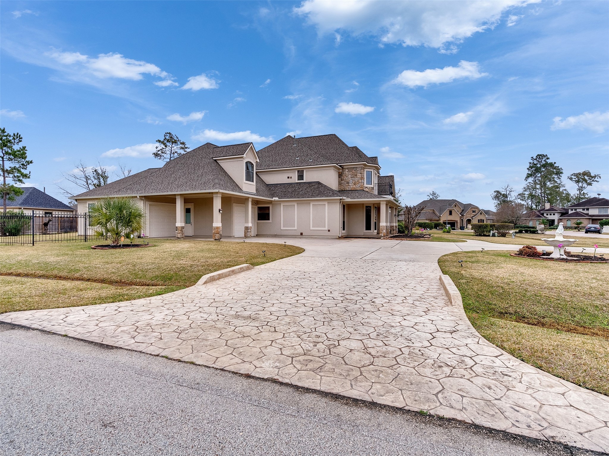 6914 Sandwedge Point Court Spring, TX 77389 - Photo 46 of 50 This photo showcases a spacious two-story home with a stone and stucco exterior. It features a large, stamped concrete driveway leading to a covered carport. The front yard is well-maintained, with a few trees and shrubs, providing a welcoming curb appeal. The neighborhood appears quiet and residential, with similar well-kept homes nearby.