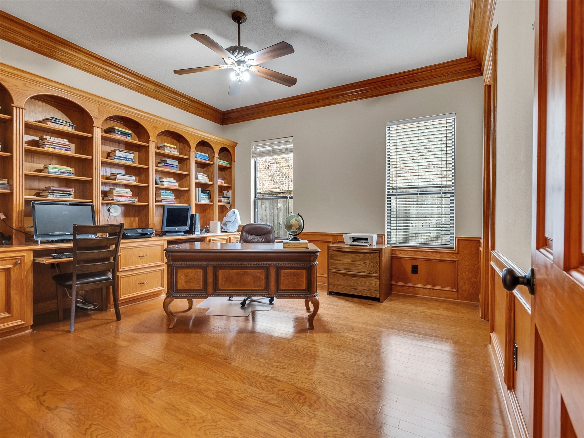 6914 Sandwedge Point Court Spring, TX 77389 - Photo 8 of 50 This spacious home office features elegant wood paneling, built-in bookshelves, and ample natural light from two large windows. It includes a ceiling fan and a sophisticated wood desk, creating a warm and inviting workspace.