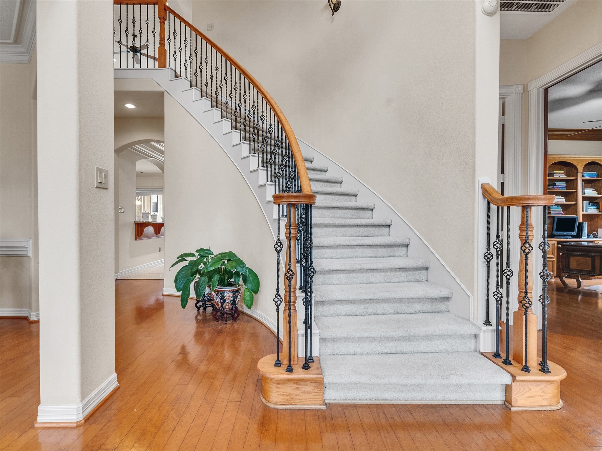 6914 Sandwedge Point Court Spring, TX 77389 - Photo 9 of 50 This photo showcases a welcoming entryway with a grand curved staircase featuring elegant wrought iron railings. The space is well-lit and has warm hardwood flooring, leading into a room with built-in shelves, ideal for an office or library.