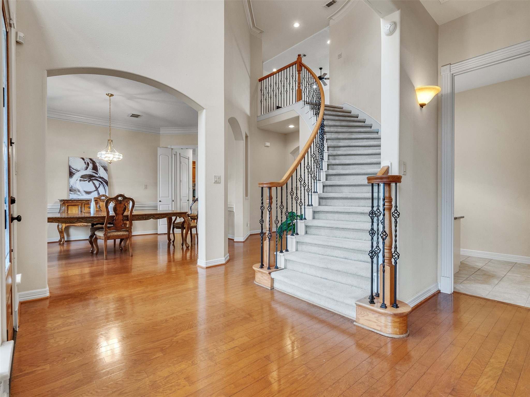 6914 Sandwedge Point Court Spring, TX 77389 - Photo 10 of 50 This elegant home features a grand curved staircase with iron balusters and a bright, open layout. The entryway showcases hardwood floors leading to a formal dining area, highlighted by an arched doorway and a stylish chandelier.