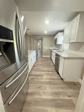 a large white kitchen with granite countertop a sink and dishwasher a stove with wooden floor