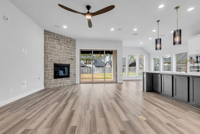 an empty room with wooden floor a fireplace a ceiling fan and windows