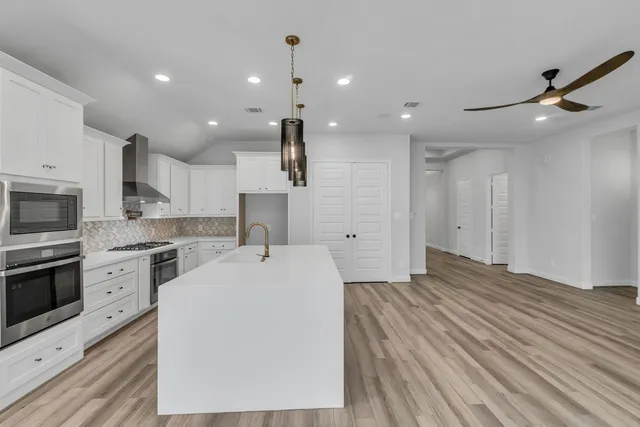 a large white kitchen with wooden floor and stainless steel appliances