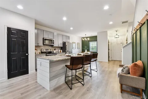 a kitchen with stainless steel appliances kitchen island granite countertop a refrigerator a stove a sink a dining table and chairs with wooden floor