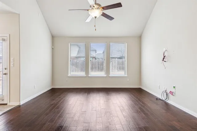 an empty room with wooden floor chandelier fan and windows