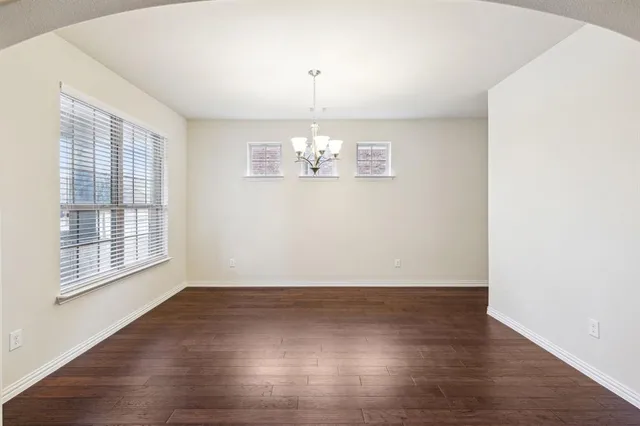 an empty room with wooden floor chandelier and windows