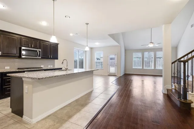 a large kitchen with stainless steel appliances a large counter top a stove a sink dishwasher a microwave oven and a refrigerator with wooden floor