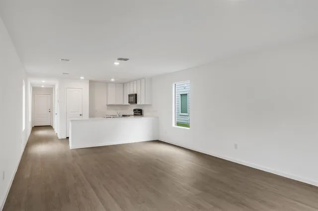 a view of an empty room with kitchen and window