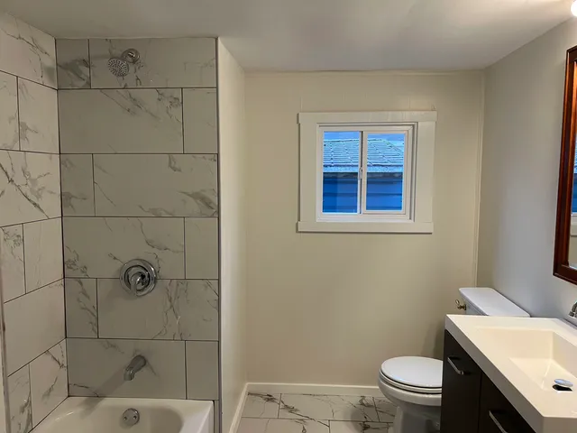 a bathroom with a toilet a sink a window and shower