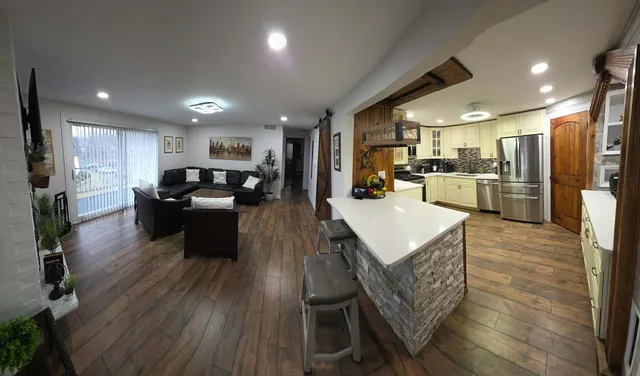 a kitchen with stainless steel appliances granite countertop a refrigerator a sink dishwasher a stove and a dining table with wooden floor