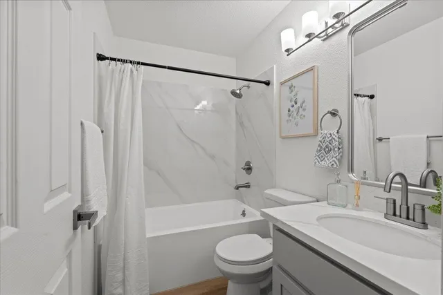 a bathroom with a granite countertop sink a toilet a mirror a vanity and shower