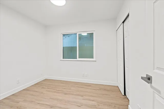 a view of an empty room with wooden floor and a window
