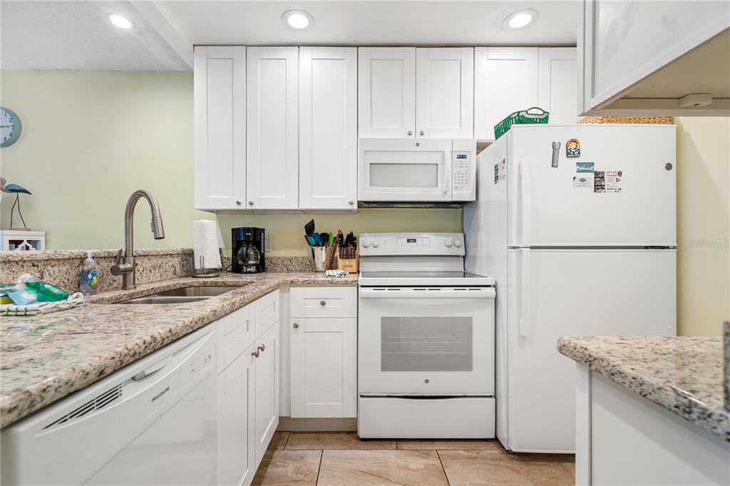 230 Medallion Boulevard, Unit E Madeira Beach, FL 33708 - Photo 9 of 35 a kitchen with granite countertop white cabinets and white appliances