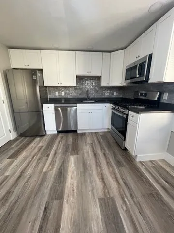 a large kitchen with granite countertop a refrigerator a sink dishwasher a stove and white countertops with wooden floor