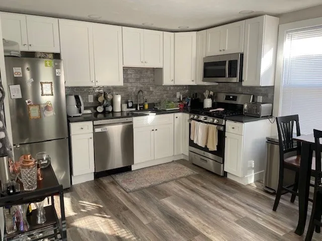 a kitchen with stainless steel appliances granite countertop a stove top oven a sink a refrigerator and white cabinets