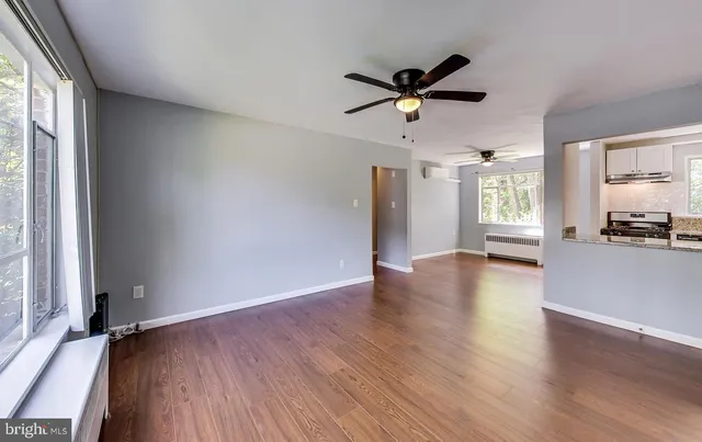 an empty room with wooden floor a ceiling fan and windows