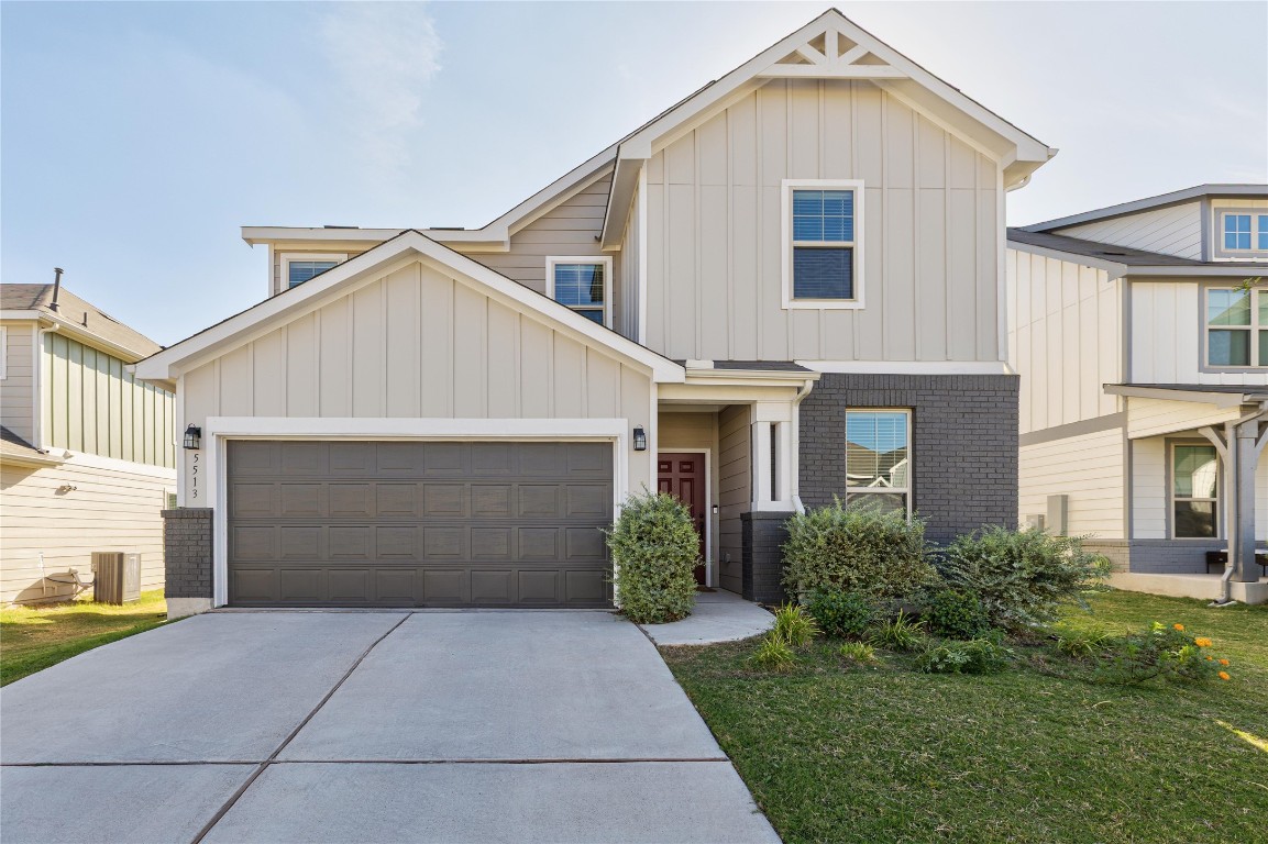 View of front facade with board and batten siding, brick siding, concrete driveway, a front lawn, and an attached garage