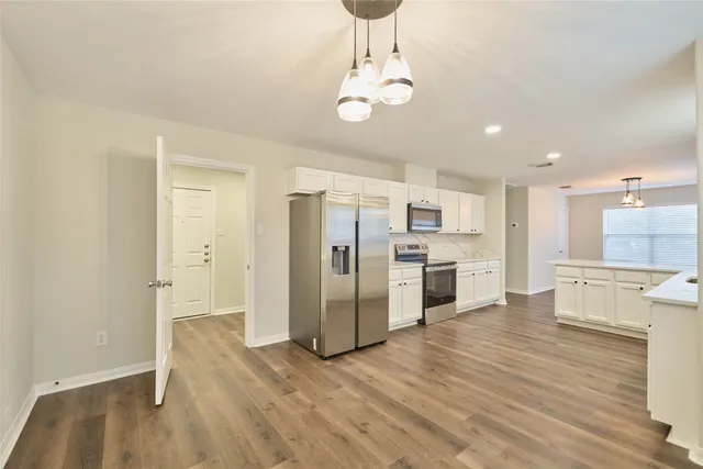 a view of a kitchen with stainless steel appliances granite countertop a dishwasher a stove a refrigerator and white cabinets with wooden floor