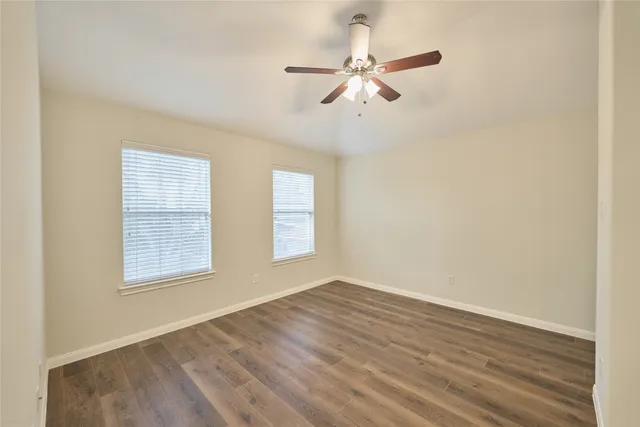 an empty room with wooden floor fan and windows