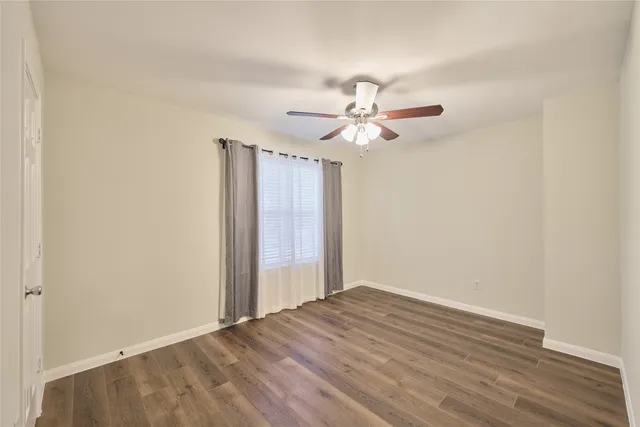 an empty room with wooden floor fan and windows