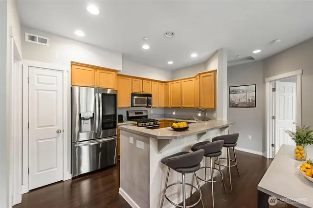 a kitchen with stainless steel appliances a refrigerator a stove a dining table and chairs with wooden floor