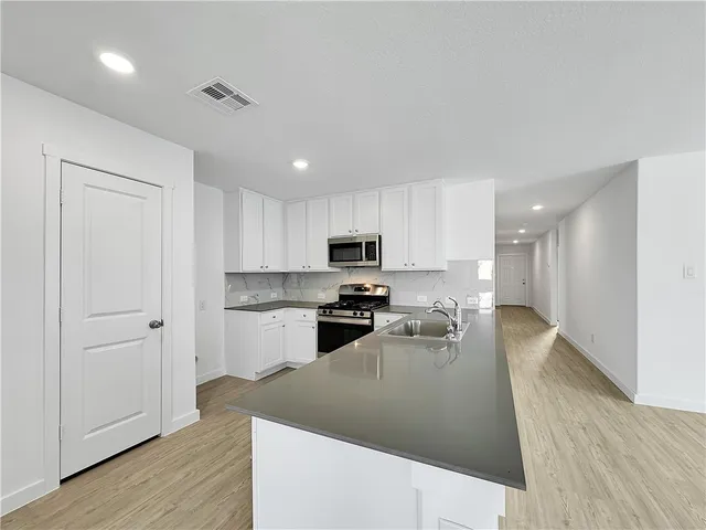 a kitchen with stainless steel appliances granite countertop a refrigerator a sink dishwasher a stove and white cabinets with wooden floor