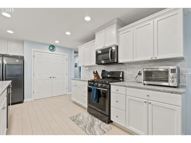 a kitchen with stainless steel appliances granite countertop a refrigerator a sink a stove a microwave and white cabinets