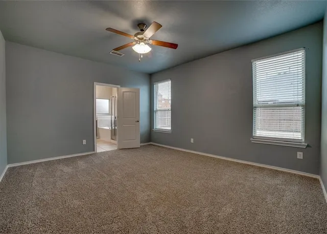 an empty room with chandelier fan and windows