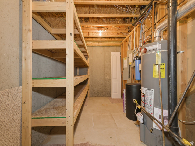 6849 North Black Powder Road Mountain Green, UT 84050 - Photo 39 of 43 Lower level utility area featuring built-in wood shelving, exposed ceiling joists, concrete flooring, and a water heater