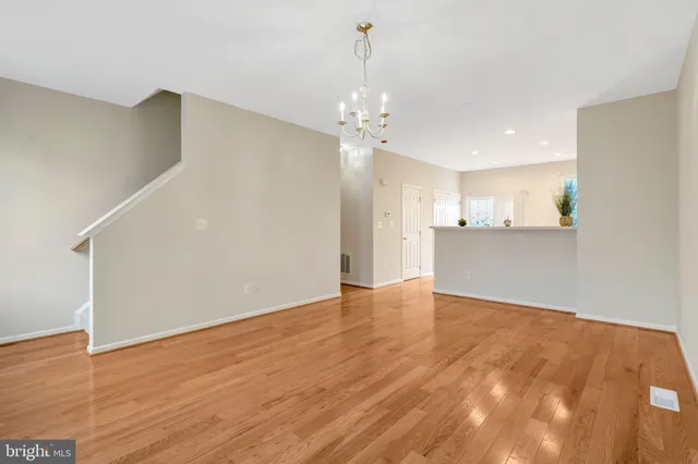 a view of an empty room with wooden floor and a kitchen