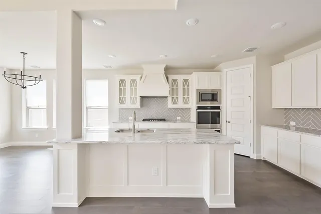 a large kitchen with kitchen island granite countertop a stove a sink a refrigerator and white cabinets with wooden floor