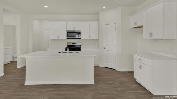 a kitchen with stainless steel appliances a stove top oven a sink a refrigerator white cabinets and wooden floor