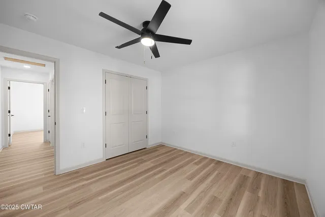 an empty room with wooden floor and a ceiling fan