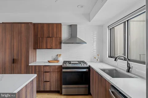 a kitchen with stainless steel appliances granite countertop a refrigerator a sink dishwasher a stove and a dining table with wooden cabinet