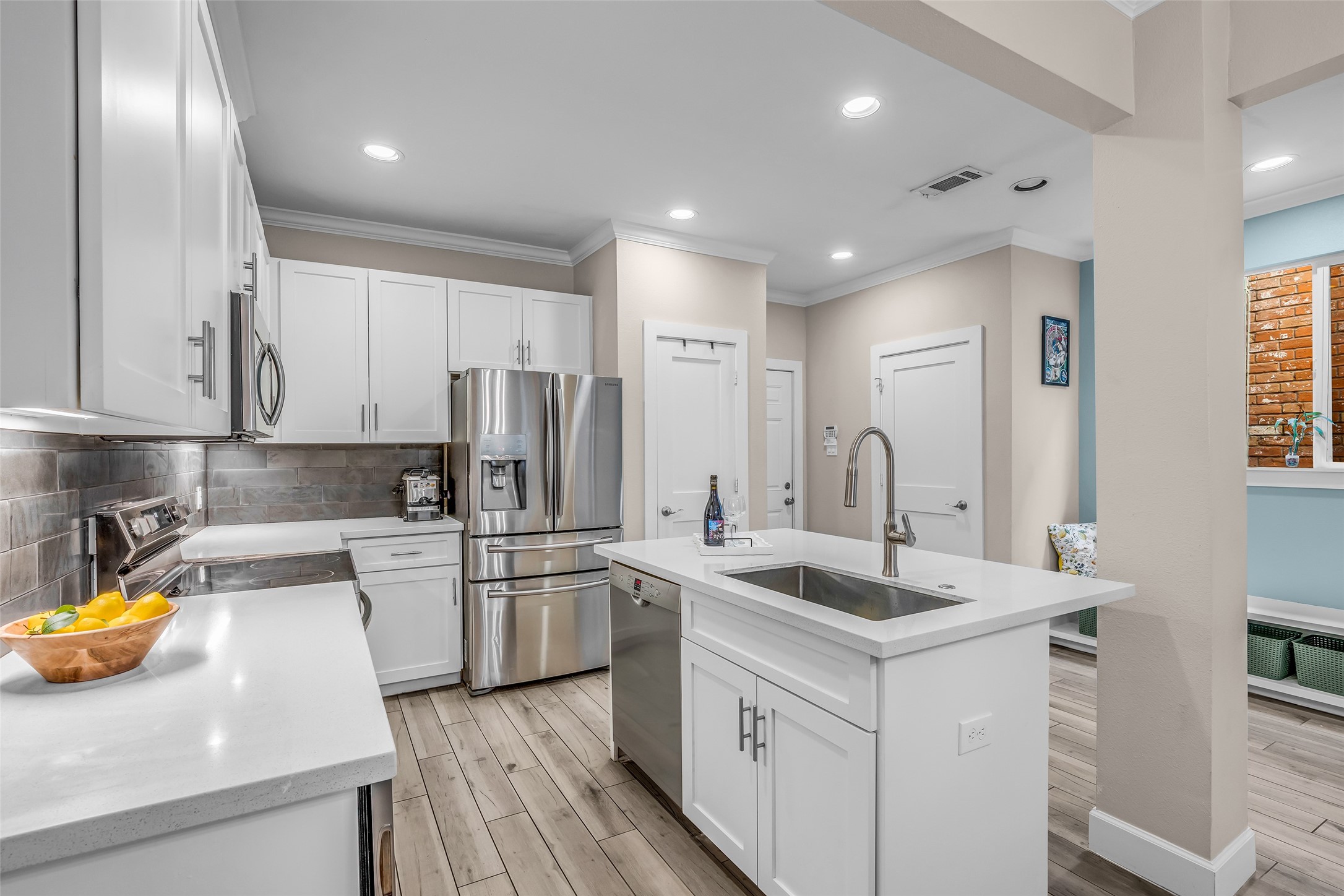 7485 Brompton Street, Unit 7485 Houston, TX 77025 - Photo 3 of 43 Bright, modern kitchen featuring white cabinets, stainless steel appliances, and a central island with a sink. The space is well-lit with recessed lighting and has a sleek, contemporary feel with light wood look tile flooring.